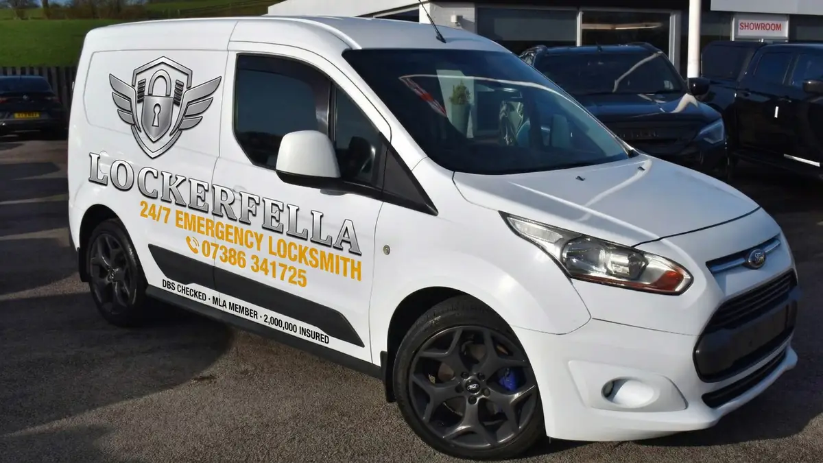 Sean's Lockerfella van: white Ford Transit Connect with chrome winged padlock badge, '24/7 Emergency Locksmith' livery, and the phone number 07386 341725 in amber