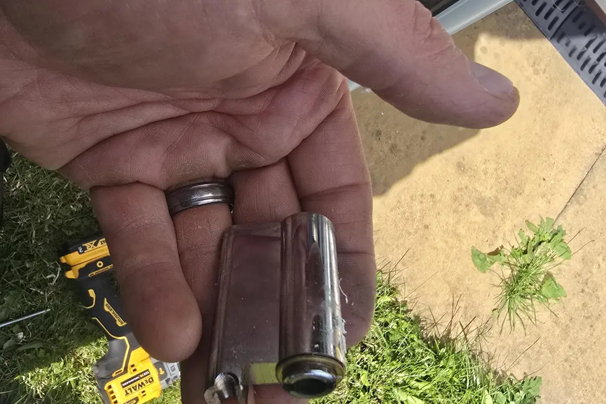 The brass euro cylinder Sean removed from a burgled home in Codsall, snapped clean across the body, held in his bare hand over the front garden with his DeWalt drill on the grass beside it, showing how a basic cylinder with no anti-snap protection fails the moment a burglar attacks it