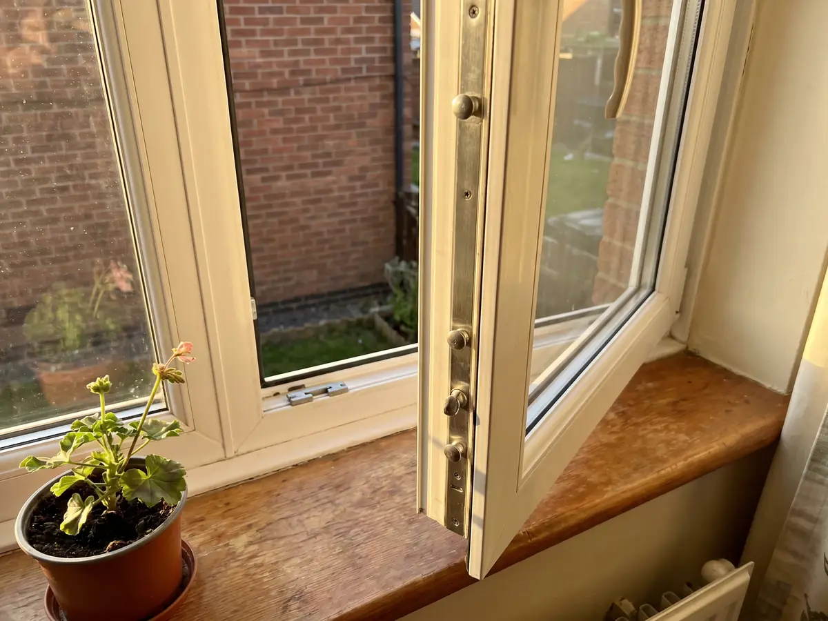 Interior view of a uPVC casement window in a Tipton home opened a little to reveal the espagnolette strip with mushroom cams along the opening edge, a geranium on the windowsill