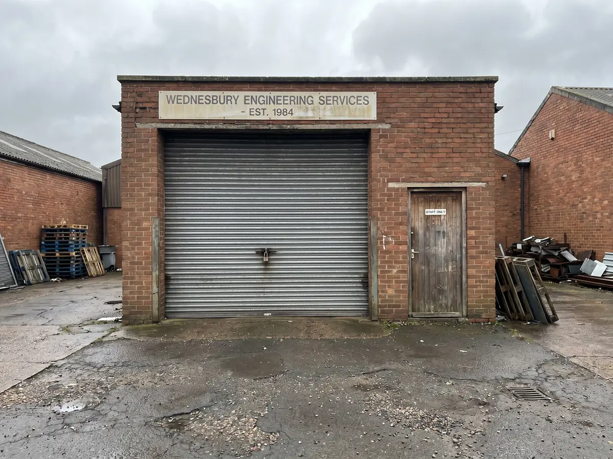 A modest single-storey commercial unit on a Wednesbury industrial estate with a roller shutter, brick walls and a Wednesbury Engineering Services sign above
